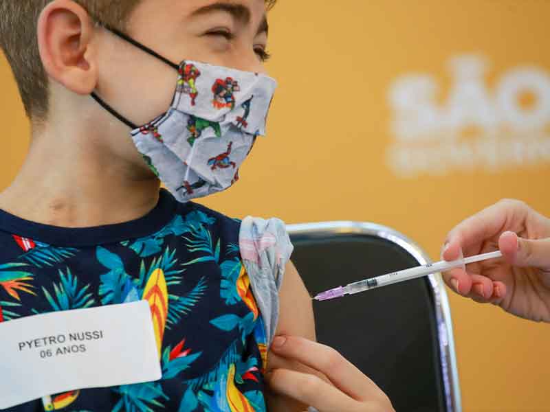 Criança, usando máscara colorida com personagem, recebe a vacina pediátrica da pfizer.