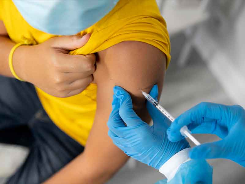 Pessoa usando máscara e usando camiseta amarela é vacinada por pessoa usando luva