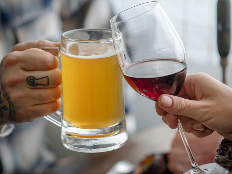 Foto mostra brinde entre com um copo de cerveja e uma taça de vinho